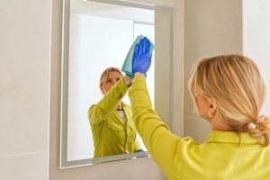 A weman is cleaning the wall mounted bathroom mirror